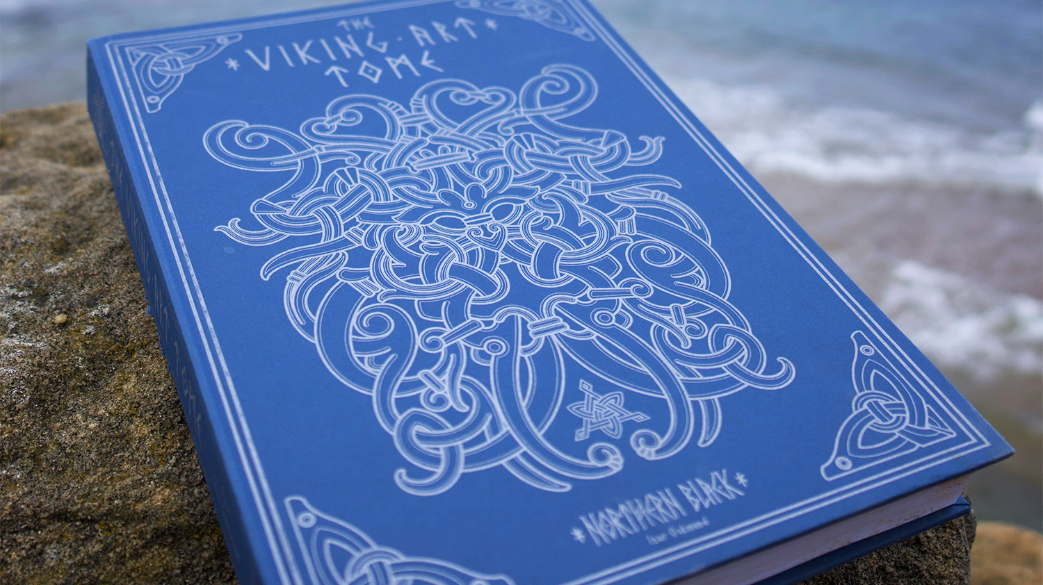 Blue book on a beach stone. Contains everything you need to know about Viking Art.
