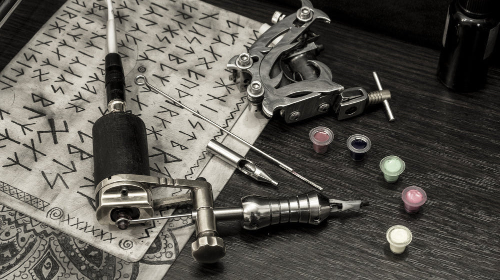 Tattoo machine with needles, ink cups, and Norse runes