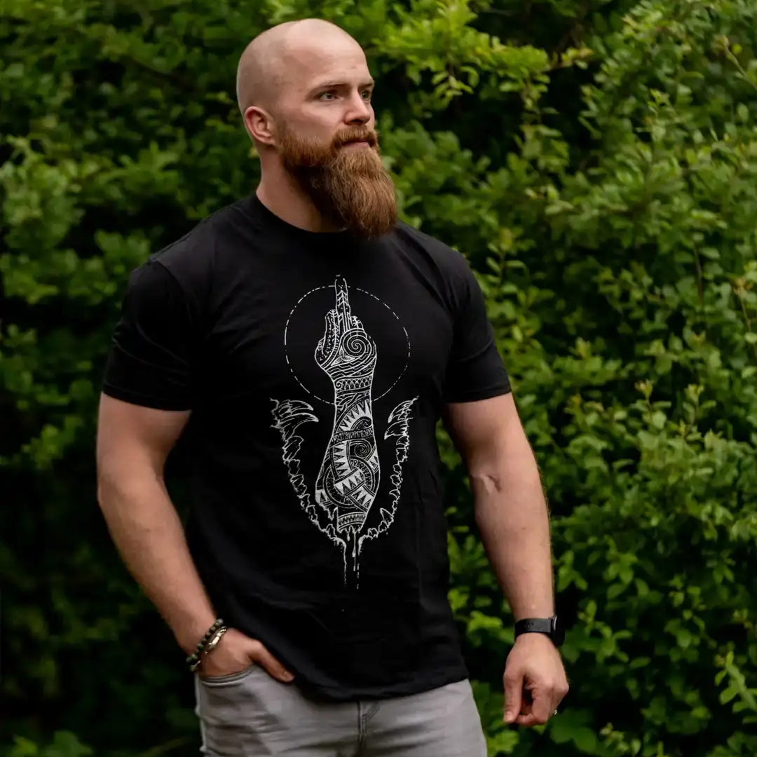 Man wearing black Norse-inspired t-shirt with Viking tattoo art design, standing outdoors