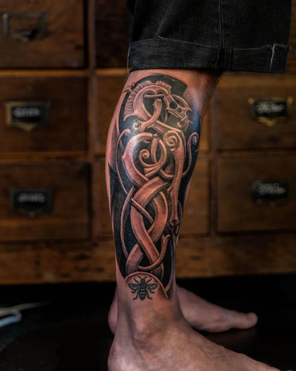 Viking-inspired leg tattoo with Norse knotwork, dragon motif, and bee detail on calf