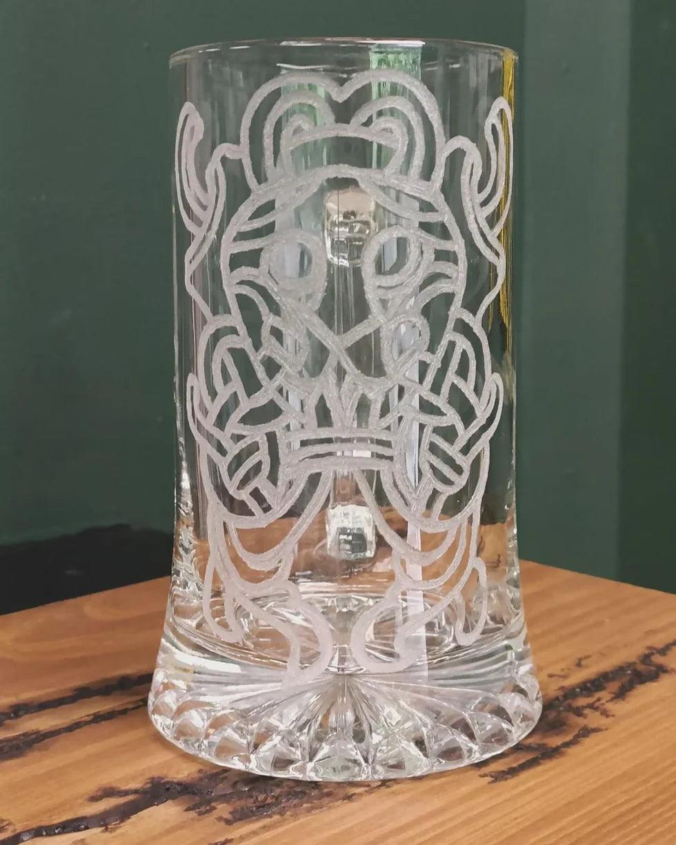 Clear glass tankard with etched Norse knotwork and Viking-inspired design, displayed on wooden surface.