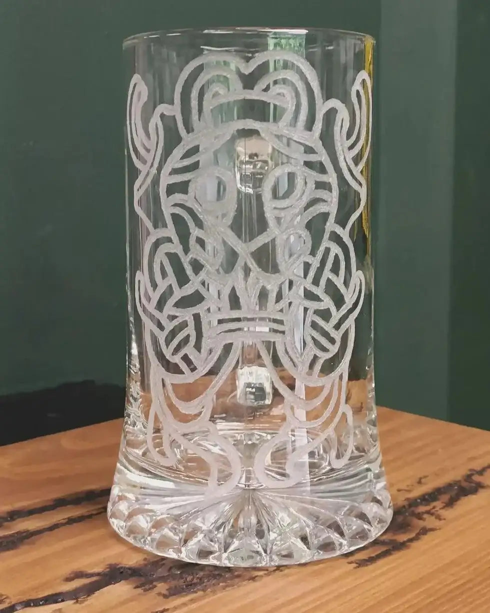 Clear glass tankard with etched Norse knotwork and Viking-inspired design, displayed on wooden surface.