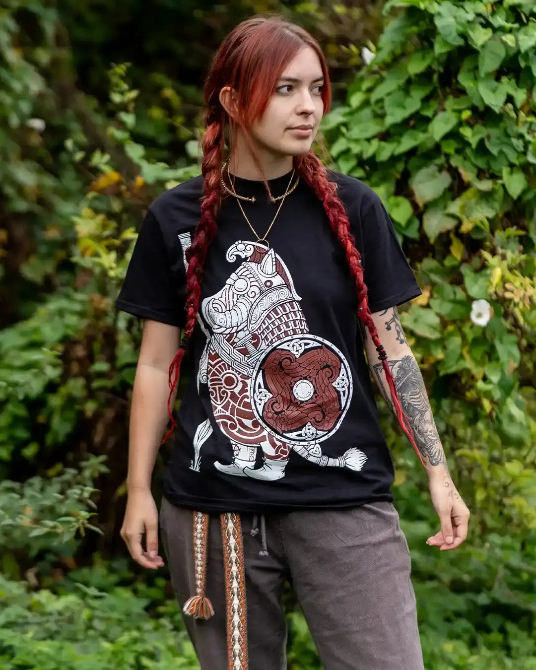 Woman wearing black Viking warrior t-shirt with Norse art, standing outdoors in greenery