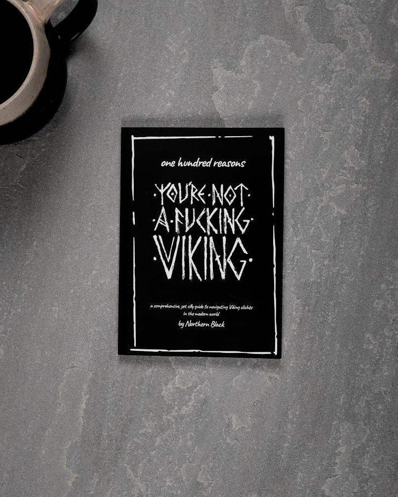 Viking-themed book titled 'You're Not a Fucking Viking' on gray surface with coffee mug