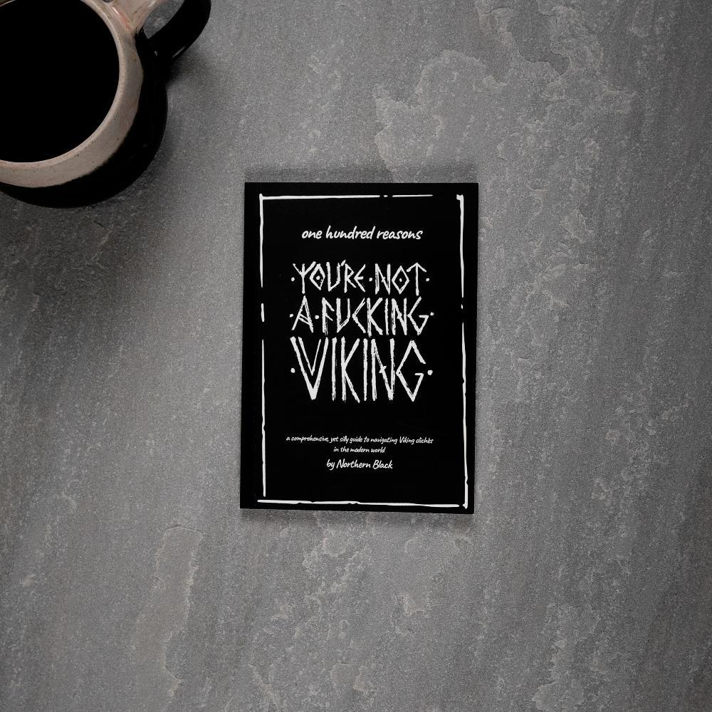 Viking-themed book titled 'You're Not a Fucking Viking' on gray surface with coffee mug