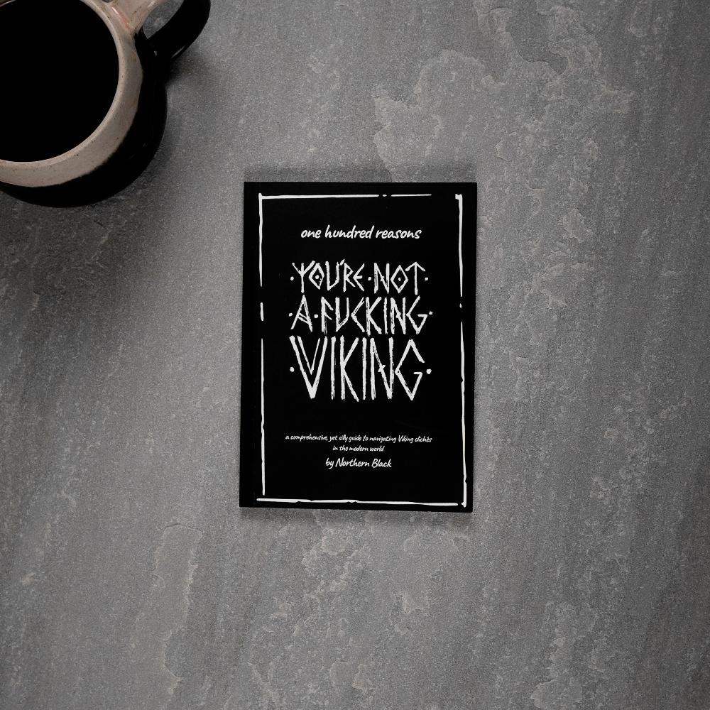 Viking-themed book titled 'You're Not a Fucking Viking' on gray surface with coffee mug