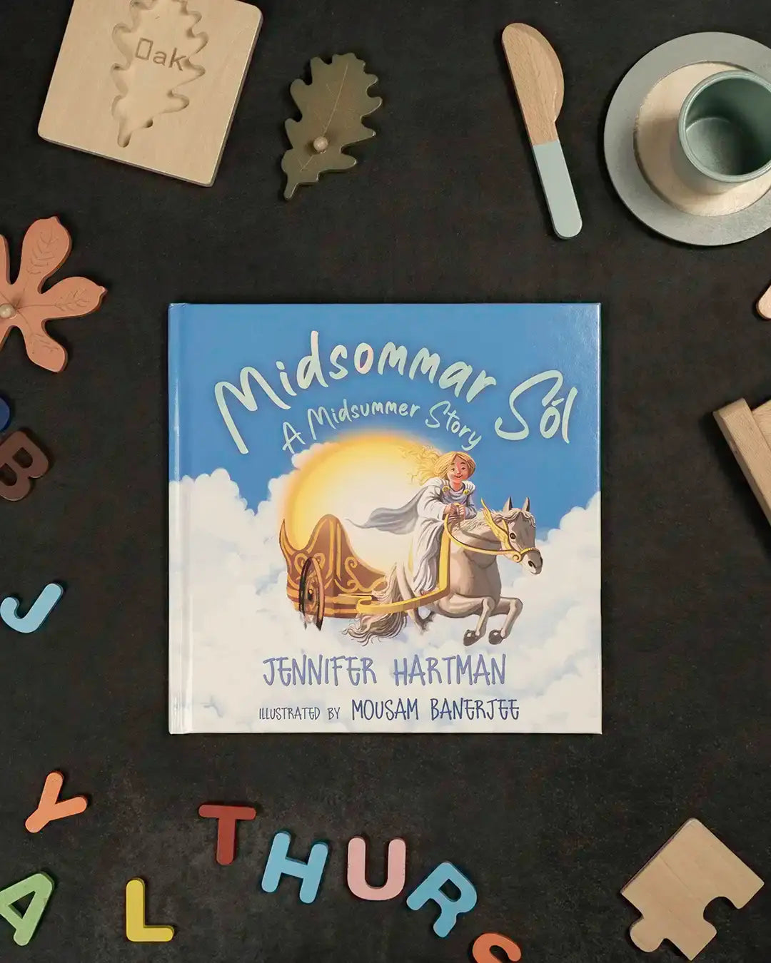 Midsommar Sol children's book with Viking-inspired art, surrounded by wooden toys and letters