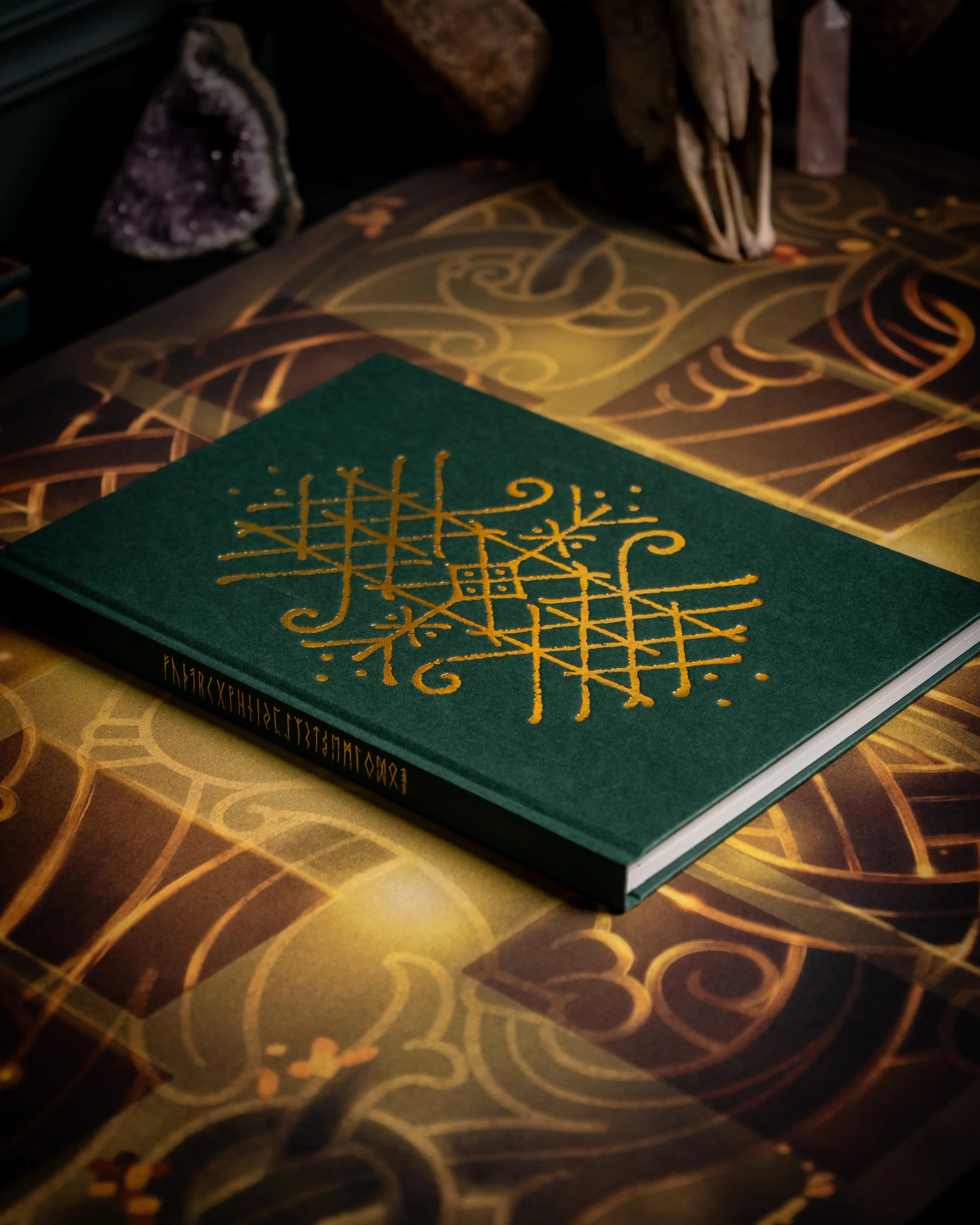 Green book with gold Norse runes and Viking knotwork, styled with amethyst and artifacts for authentic Norse design.