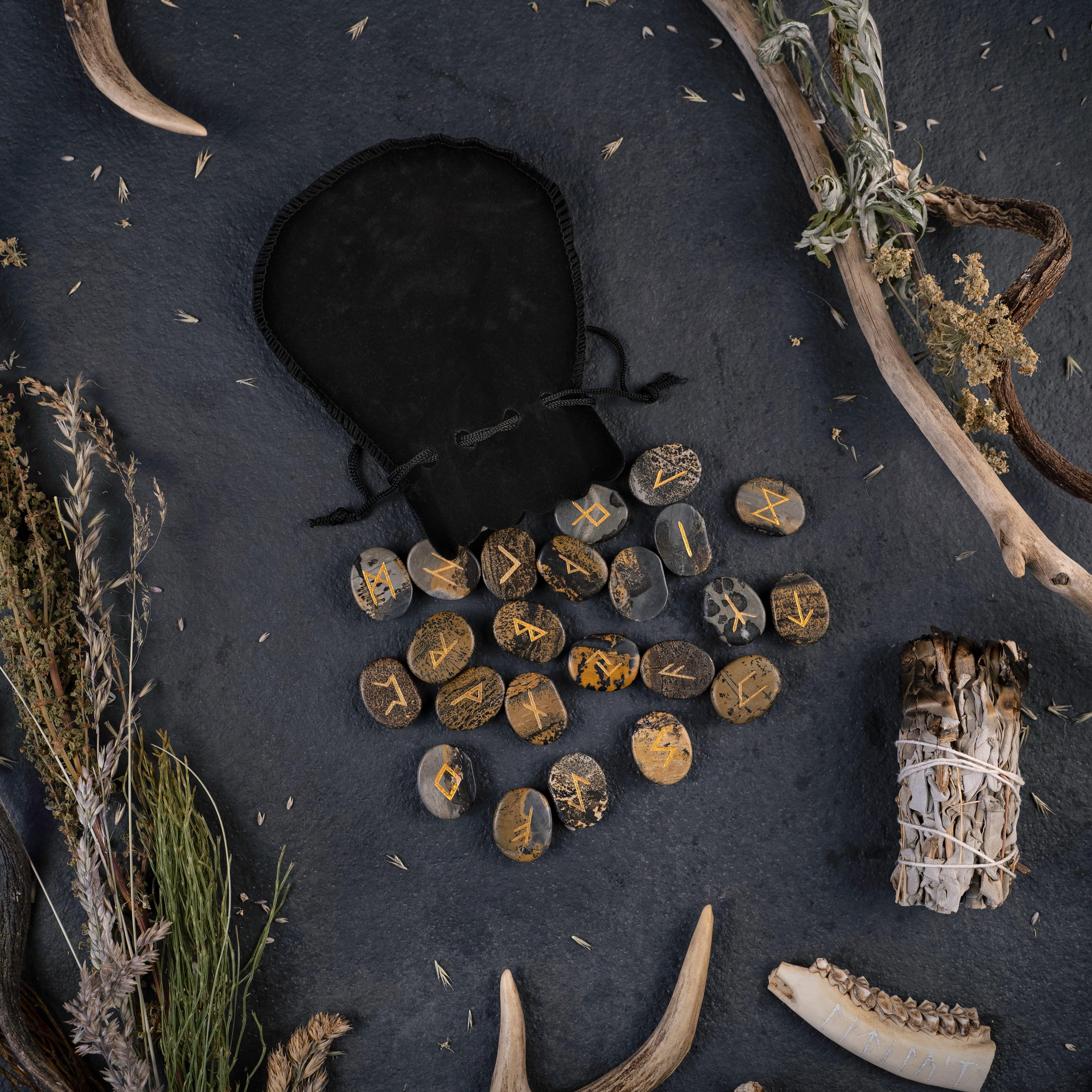 Norse rune stones with golden symbols, antlers, dried herbs, and a black pouch on dark surface