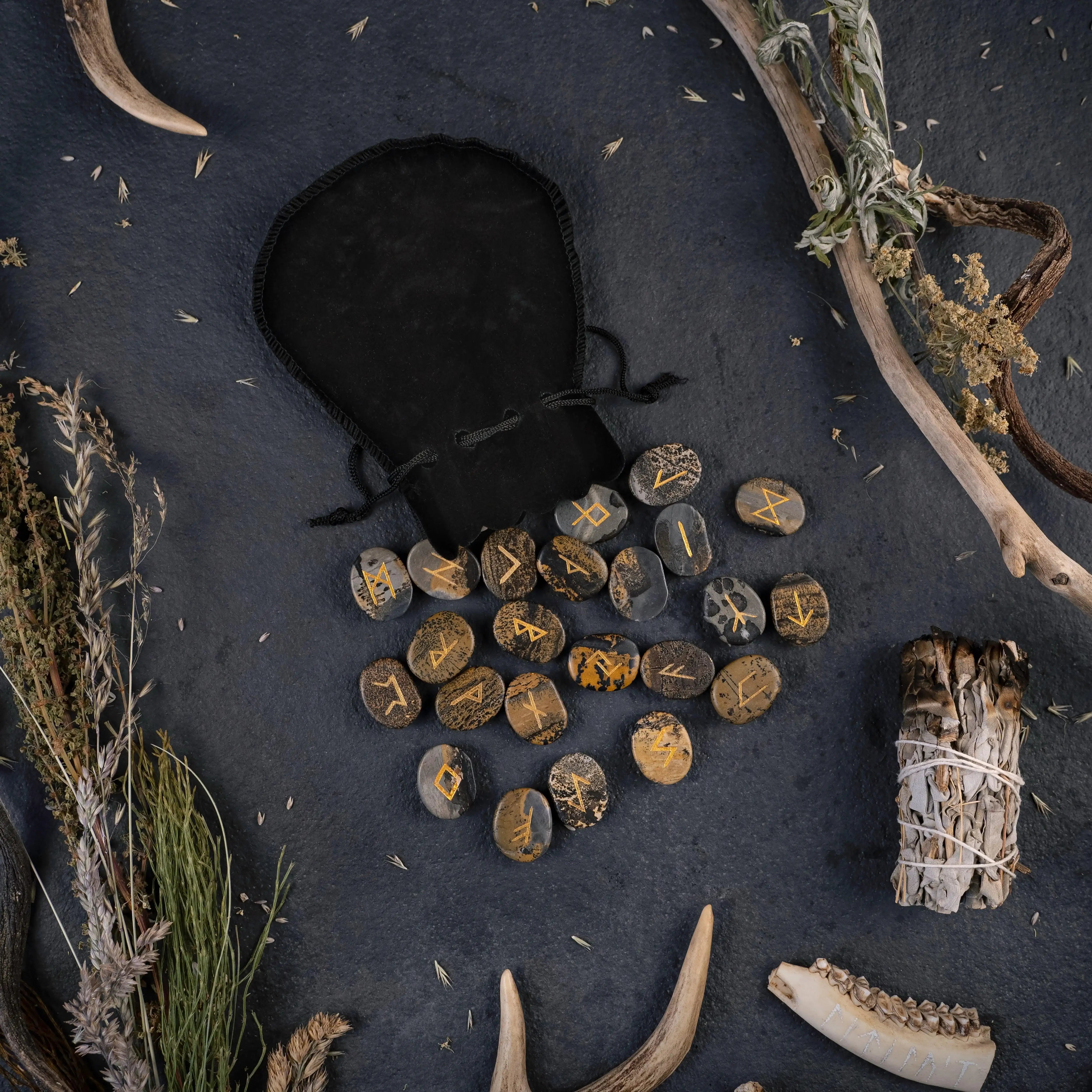 Norse rune stones with golden symbols, antlers, dried herbs, and a black pouch on dark surface