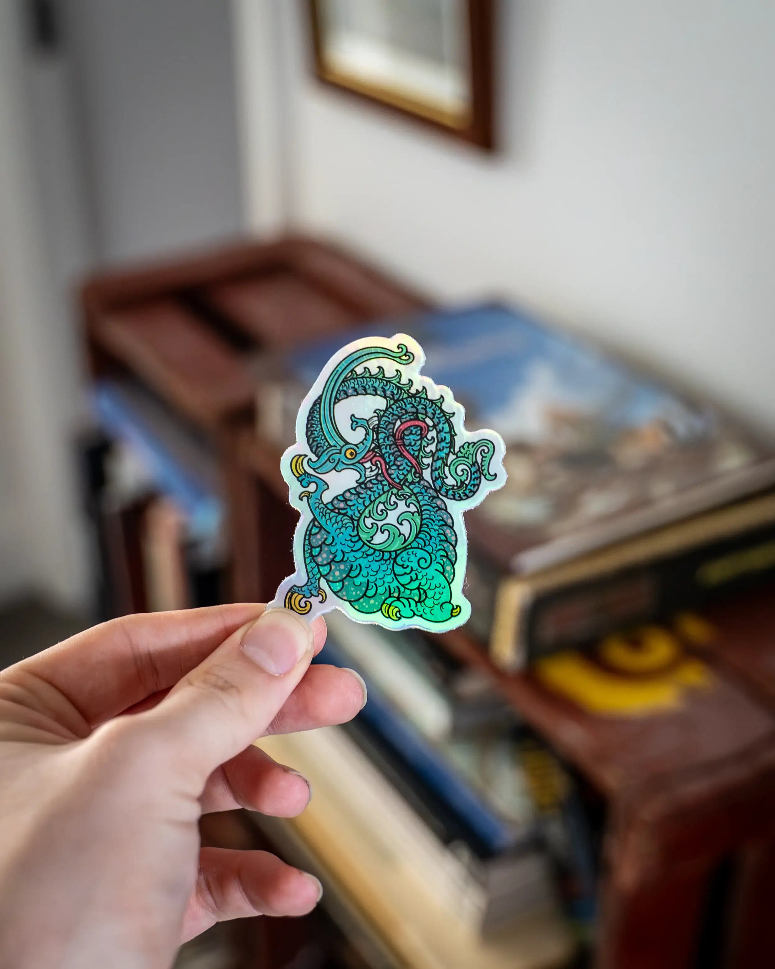 Hand holding a holographic Norse dragon sticker with intricate Viking art design