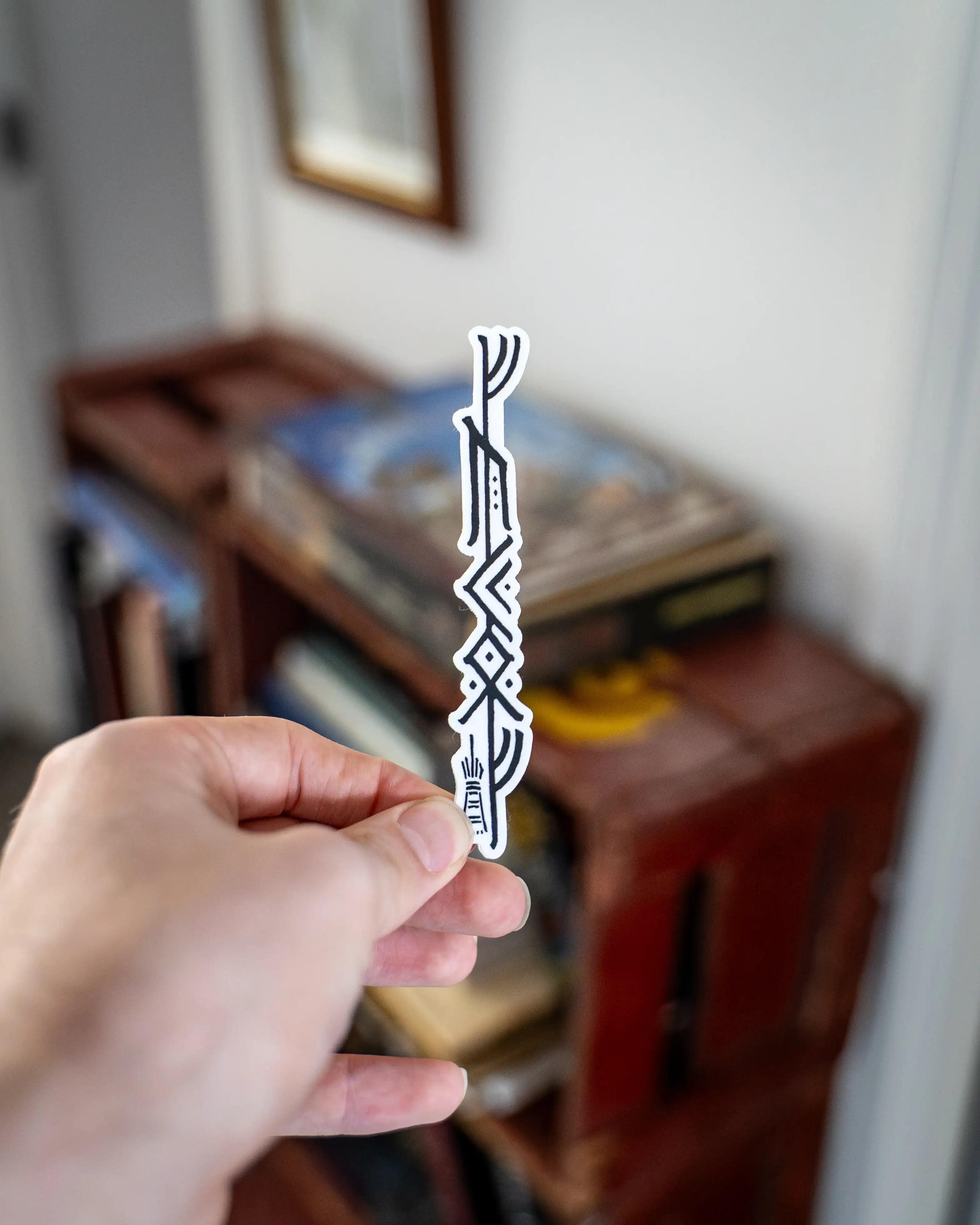 Hand holding a white Norse rune sticker with black Viking-inspired patterns, perfect for tattoo art enthusiasts.