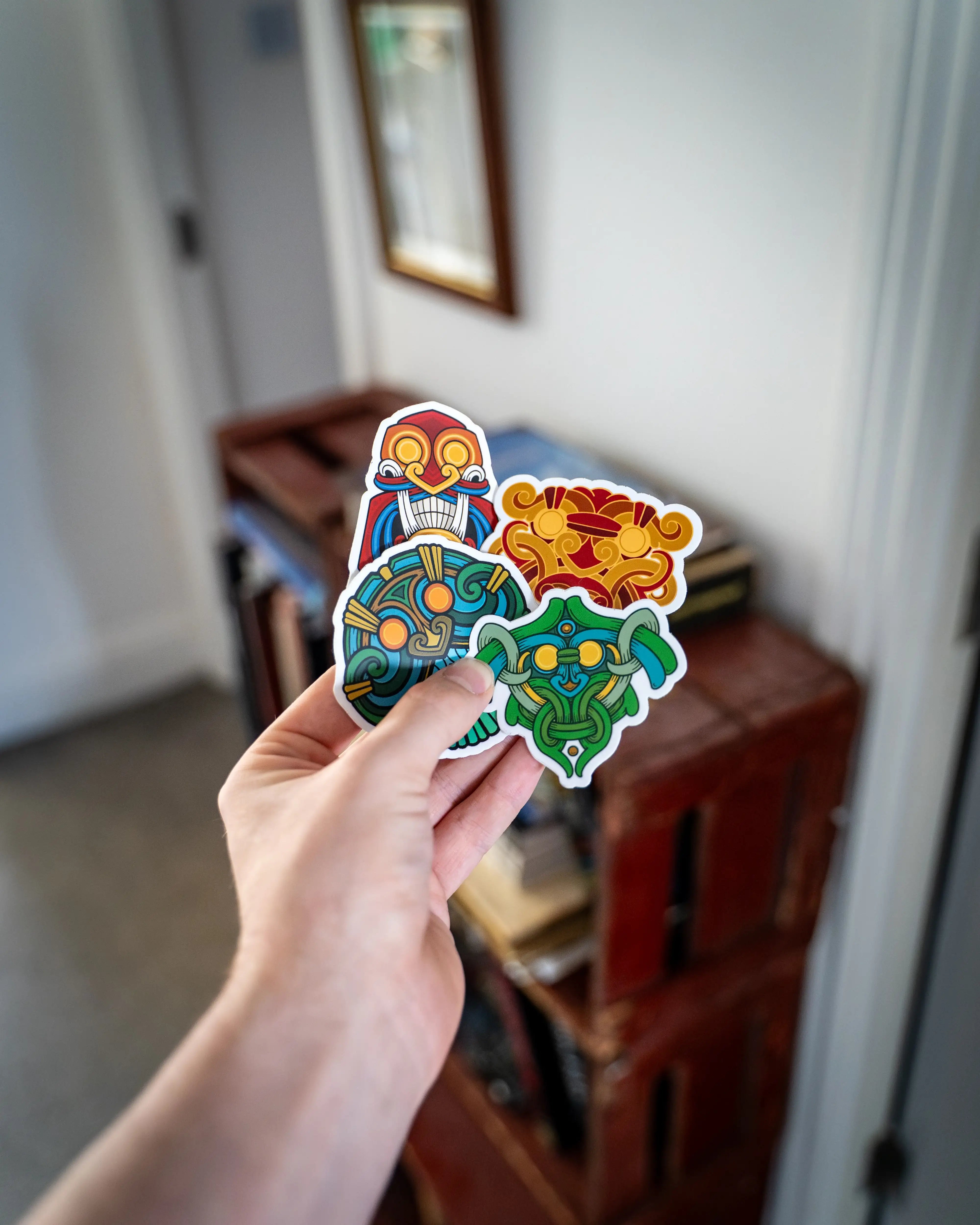 Hand holding four colorful Norse-inspired stickers with Viking art, runes, and mythological designs.