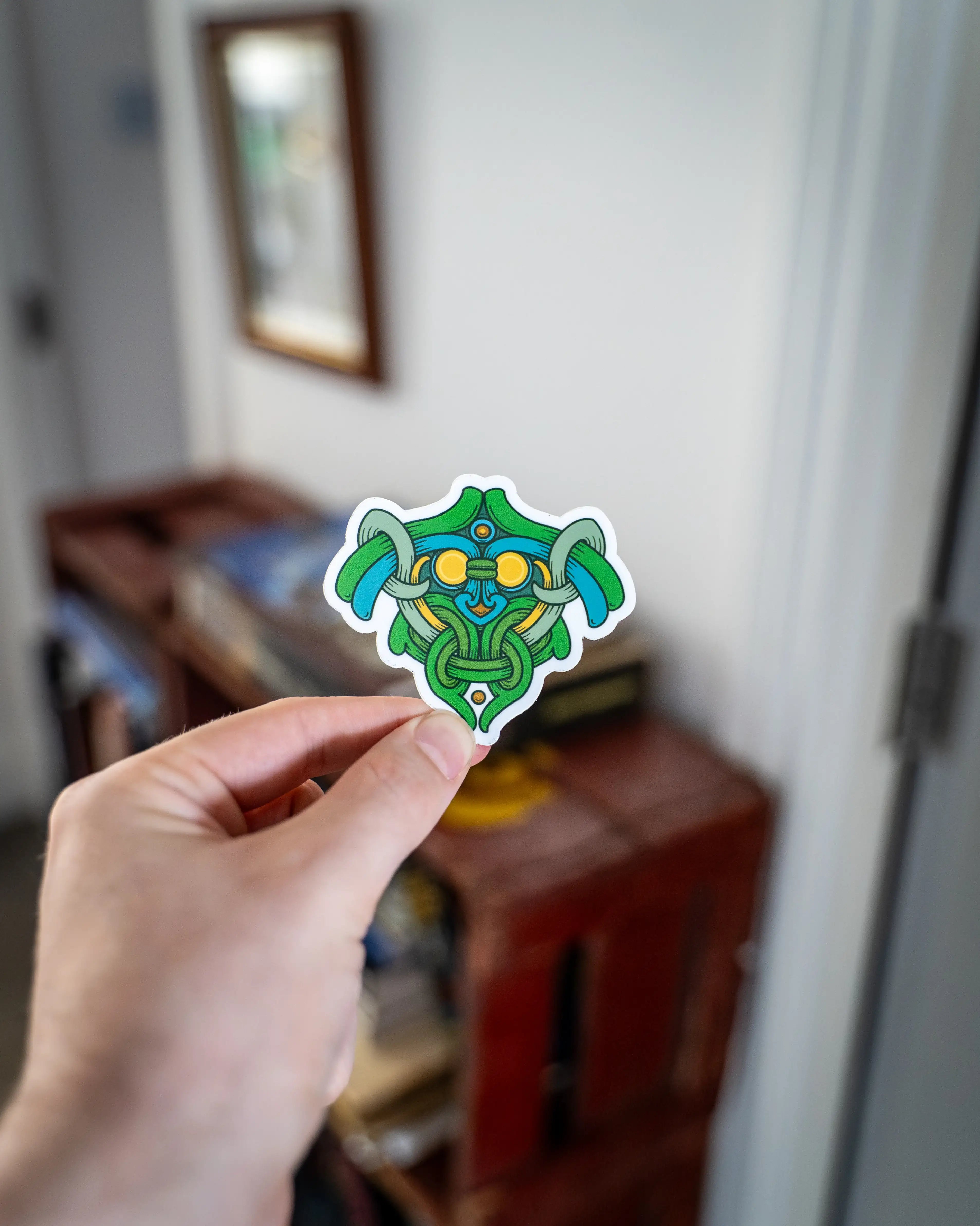 Viking-inspired sticker with green and blue Norse knotwork design held in hand