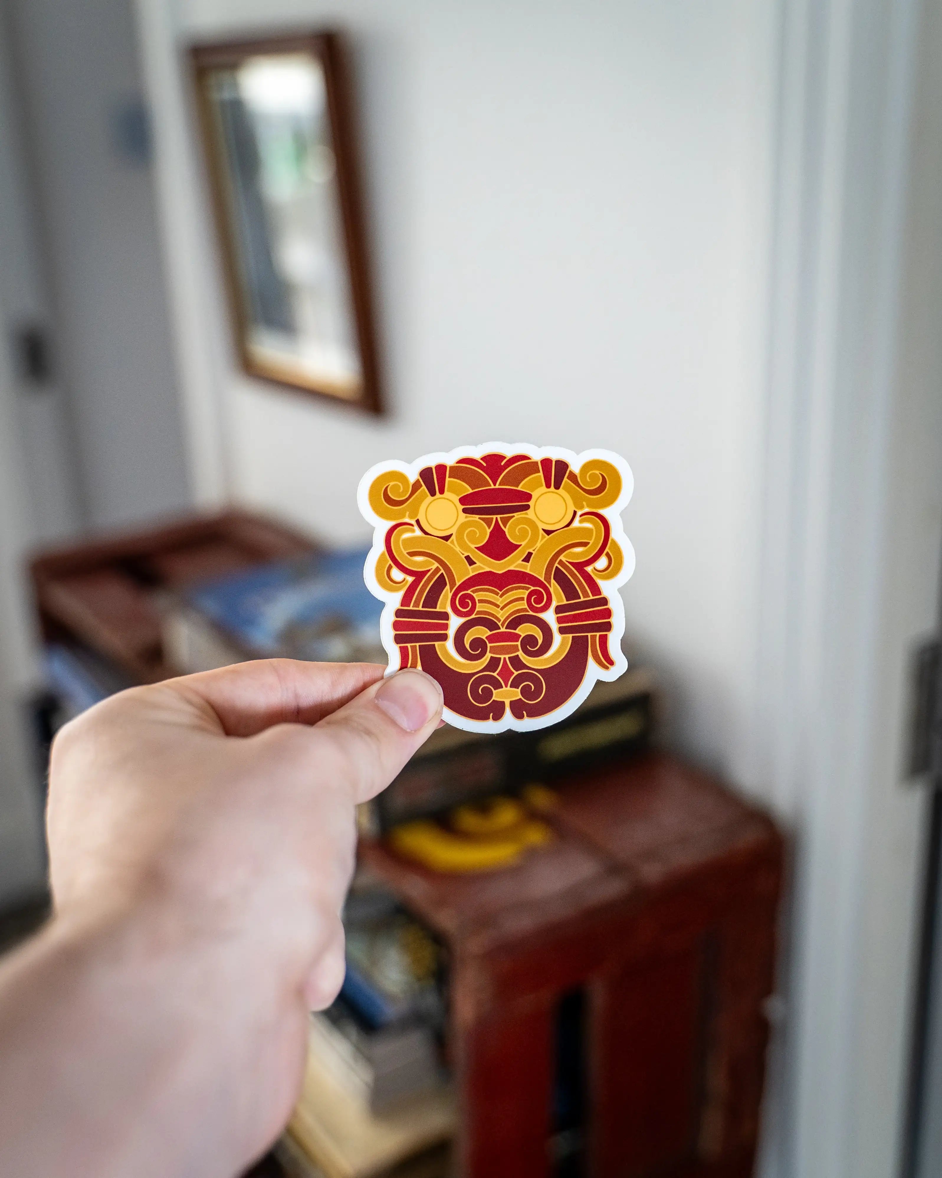 Viking-inspired sticker with red and gold Norse knotwork design held in hand