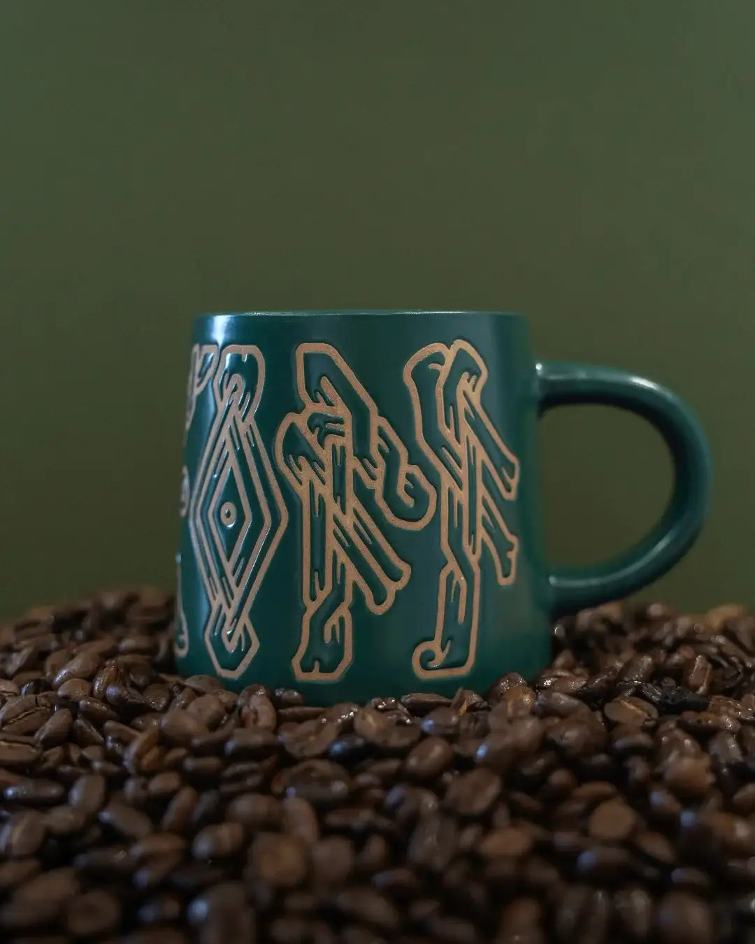Green mug with Norse Viking knotwork design, nestled in coffee beans — authentic Viking-inspired art.