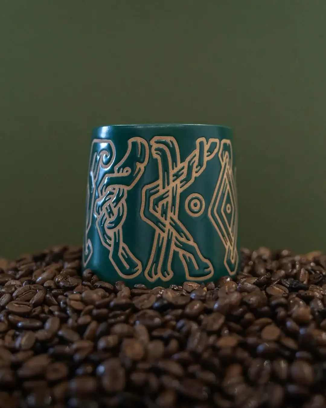 Green ceramic mug with geometric patterns on a bed of coffee beans against a green background