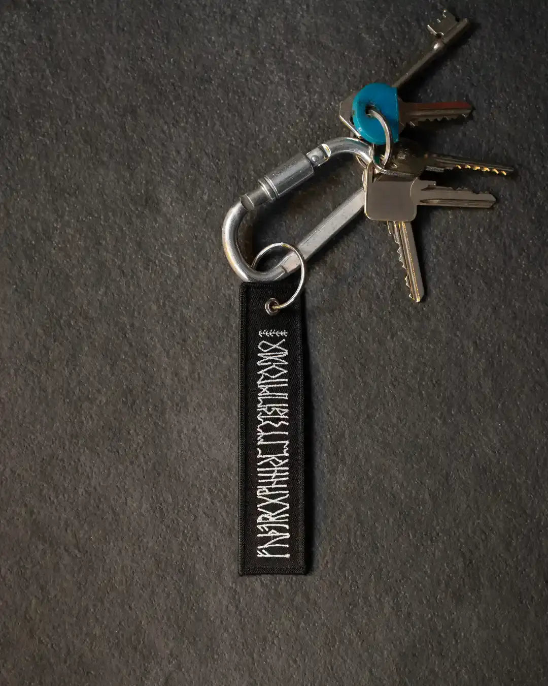 Black keychain with white Norse runes, attached to keys and carabiner on dark surface