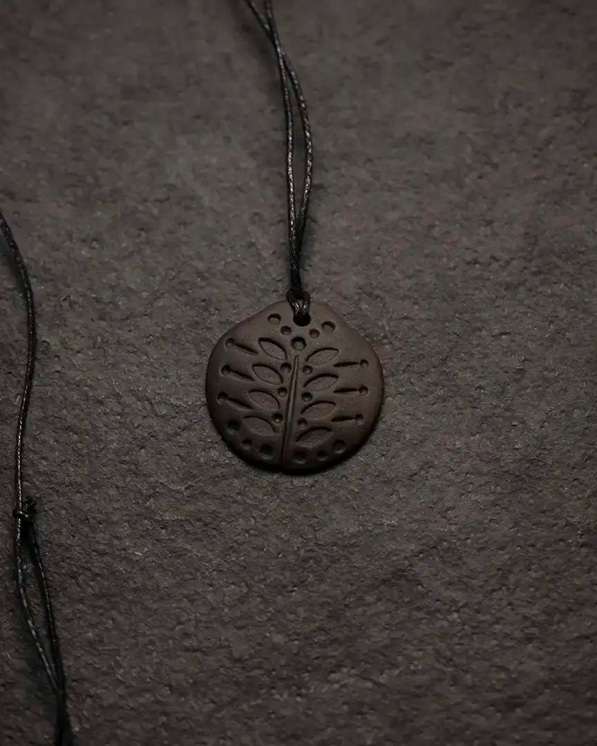 Dark Norse tree pendant with intricate leaf cutouts on cord, inspired by Viking art and runes.