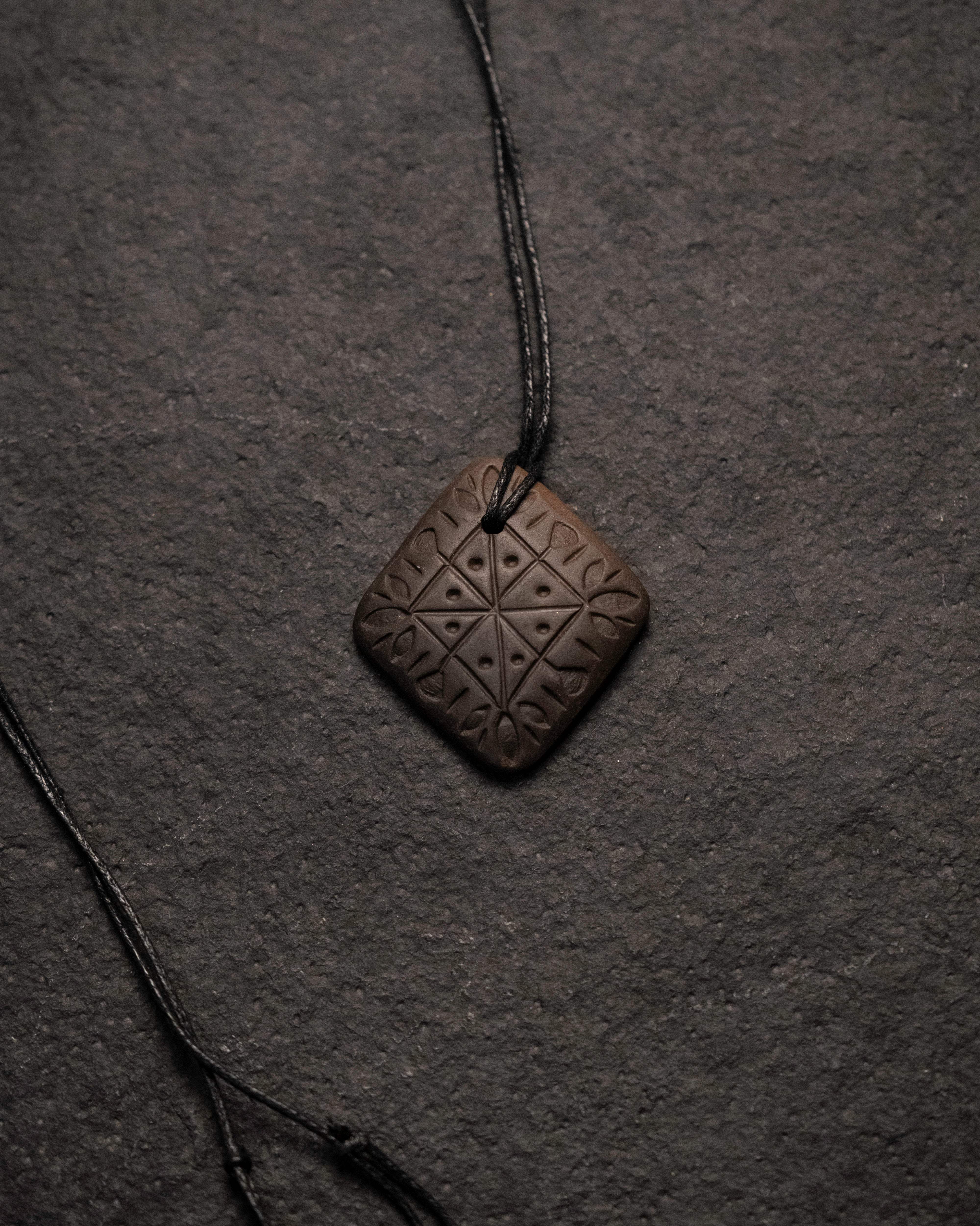Hand-carved Norse-inspired pendant with geometric runes, displayed on dark textured background.