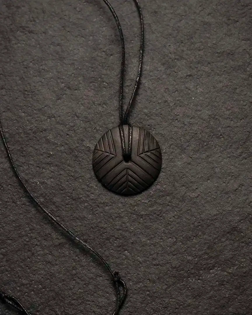 Dark Norse pendant with geometric rune-inspired design on cord, evoking Viking art and heritage.
