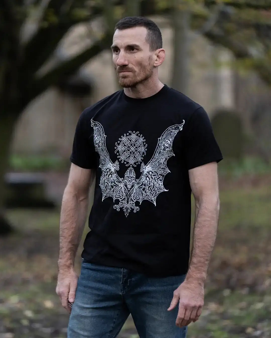 Man wearing black Norse-inspired t-shirt with intricate Viking tattoo-style bat design, outdoors