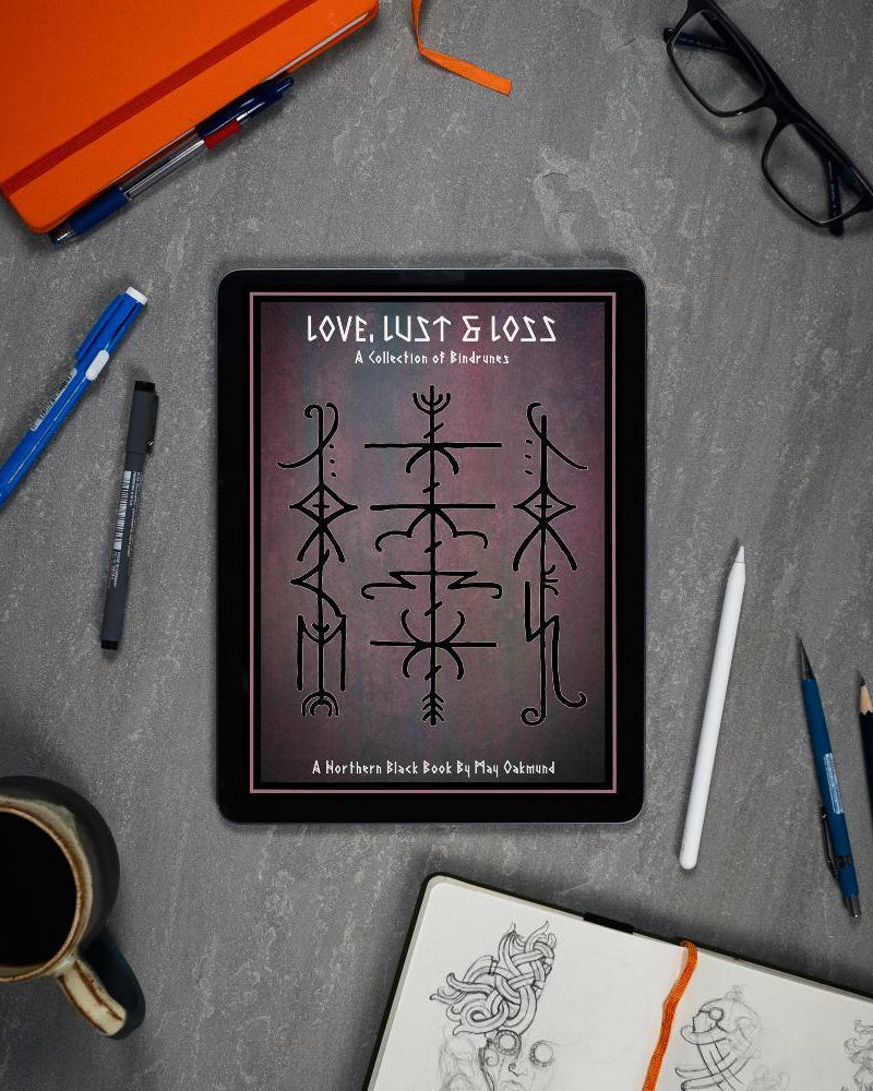 Viking rune art book on tablet, Norse-inspired designs by May Oakmund, surrounded by sketch tools and coffee