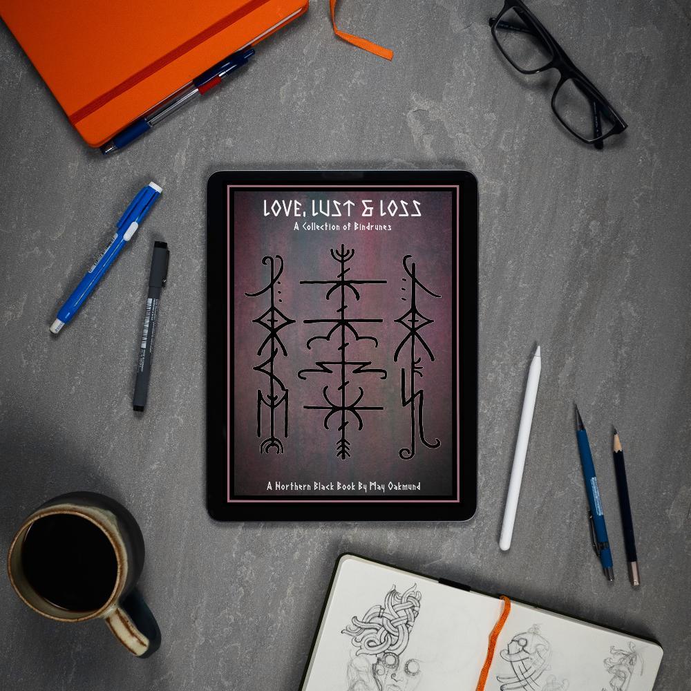 Viking rune art book on tablet, Norse-inspired designs by May Oakmund, surrounded by sketch tools and coffee