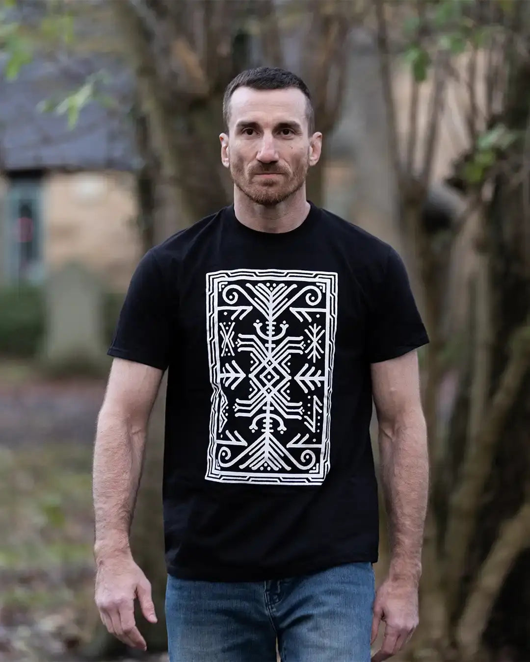 Man wearing black t-shirt with white Norse-inspired rune design, standing outdoors