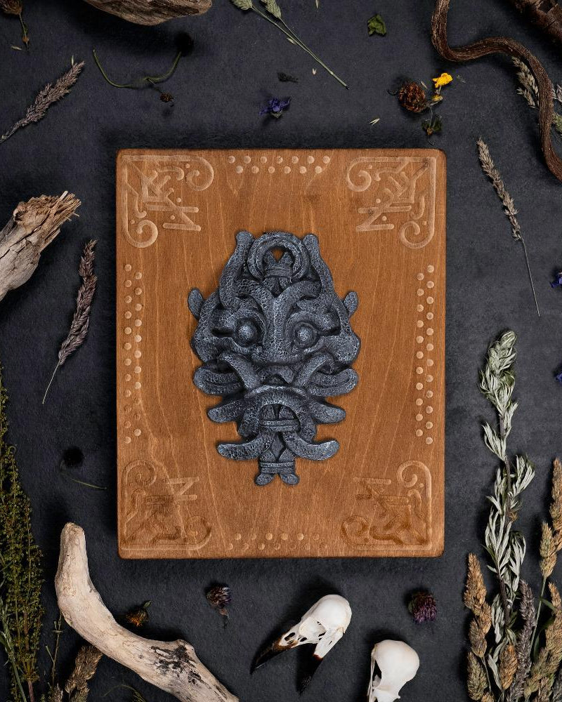 Viking-inspired wooden plaque with Norse beast carving, surrounded by dried herbs and bones