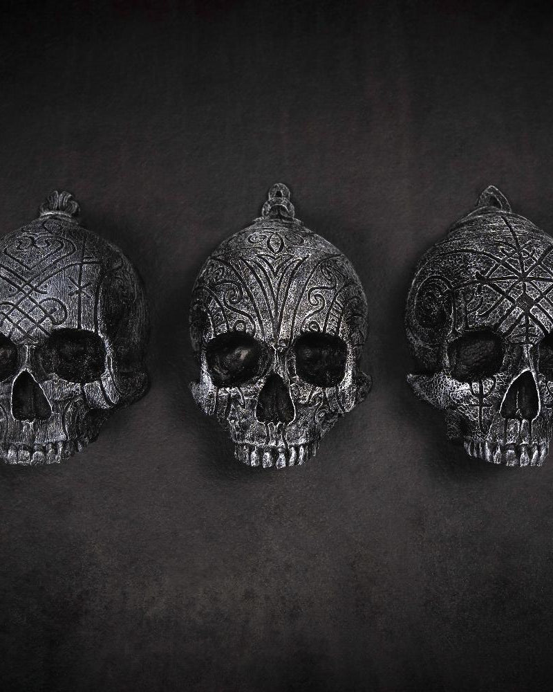 Depicting three skulls that are in a collection. They are resin human shaped skulls with runes on them, each representing one of the following: Love, Lust, Loss.