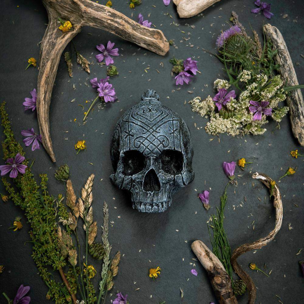 Carved Norse skull with Viking runes, surrounded by antlers, dried flowers, and herbs on dark stone.