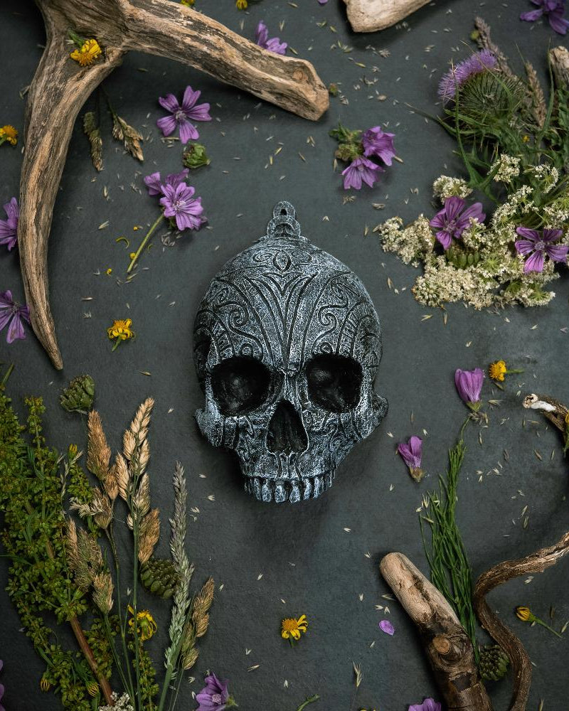 Ornate Norse skull pendant with Viking runes, surrounded by dried flowers and antlers on dark slate.