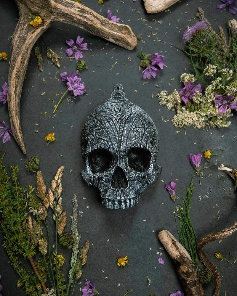 Ornate Norse skull pendant with Viking runes, surrounded by dried flowers and antlers on dark slate.