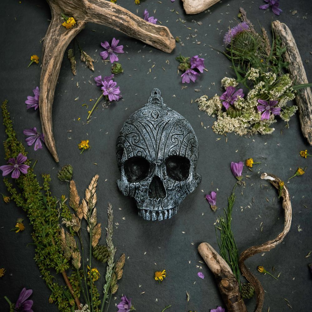 Ornate Norse skull pendant with Viking runes, surrounded by dried flowers and antlers on dark slate.