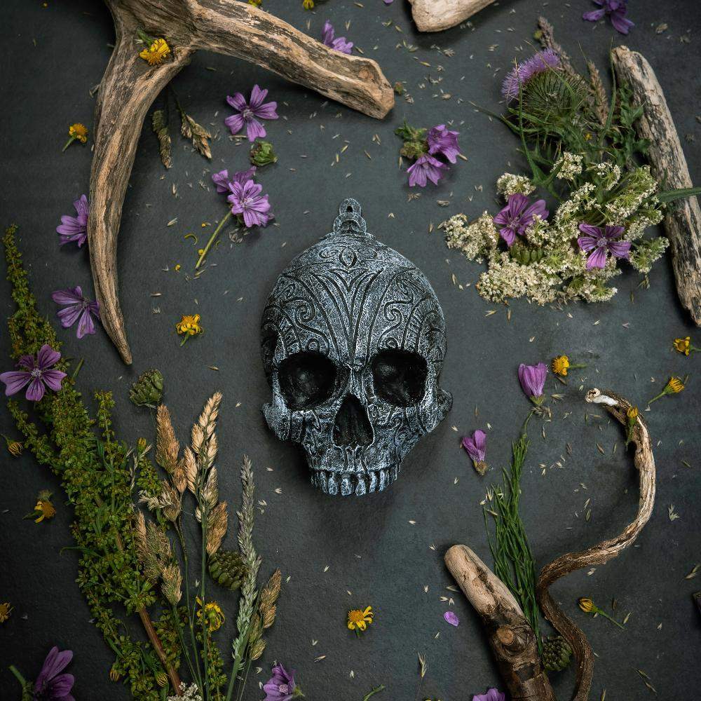 Ornate Norse skull pendant with Viking runes, surrounded by dried flowers and antlers on dark slate.
