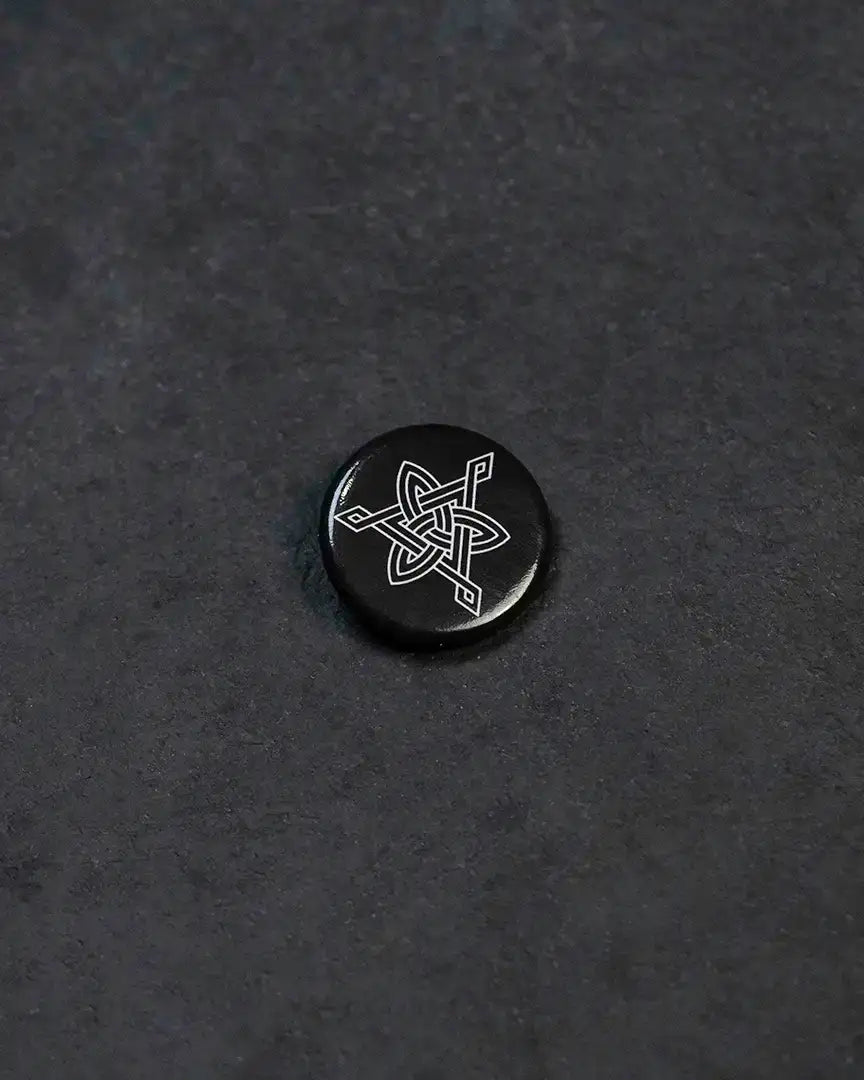 Black enamel pin with white Norse knotwork design, Viking-inspired accessory on dark textured surface
