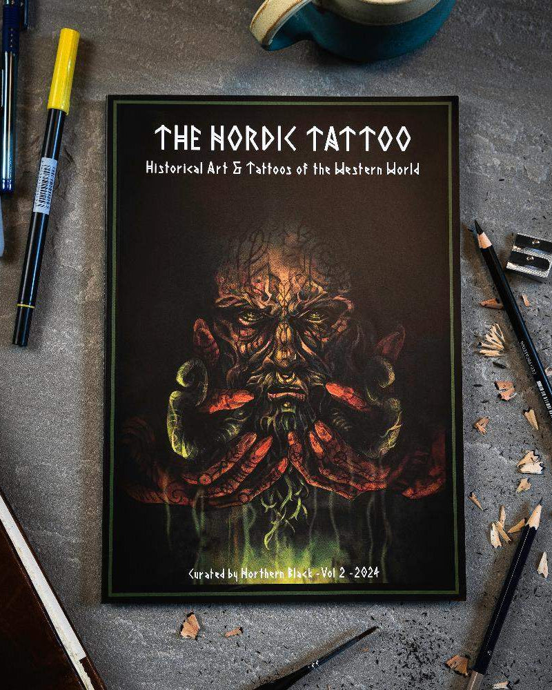 The Nordic Tattoo art book with Viking-inspired cover, surrounded by pens and pencils on a desk