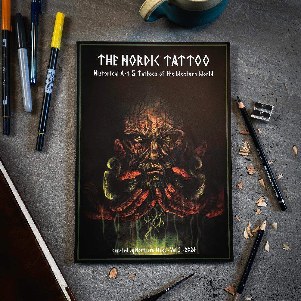 The Nordic Tattoo art book with Viking-inspired cover, surrounded by pens and pencils on a desk