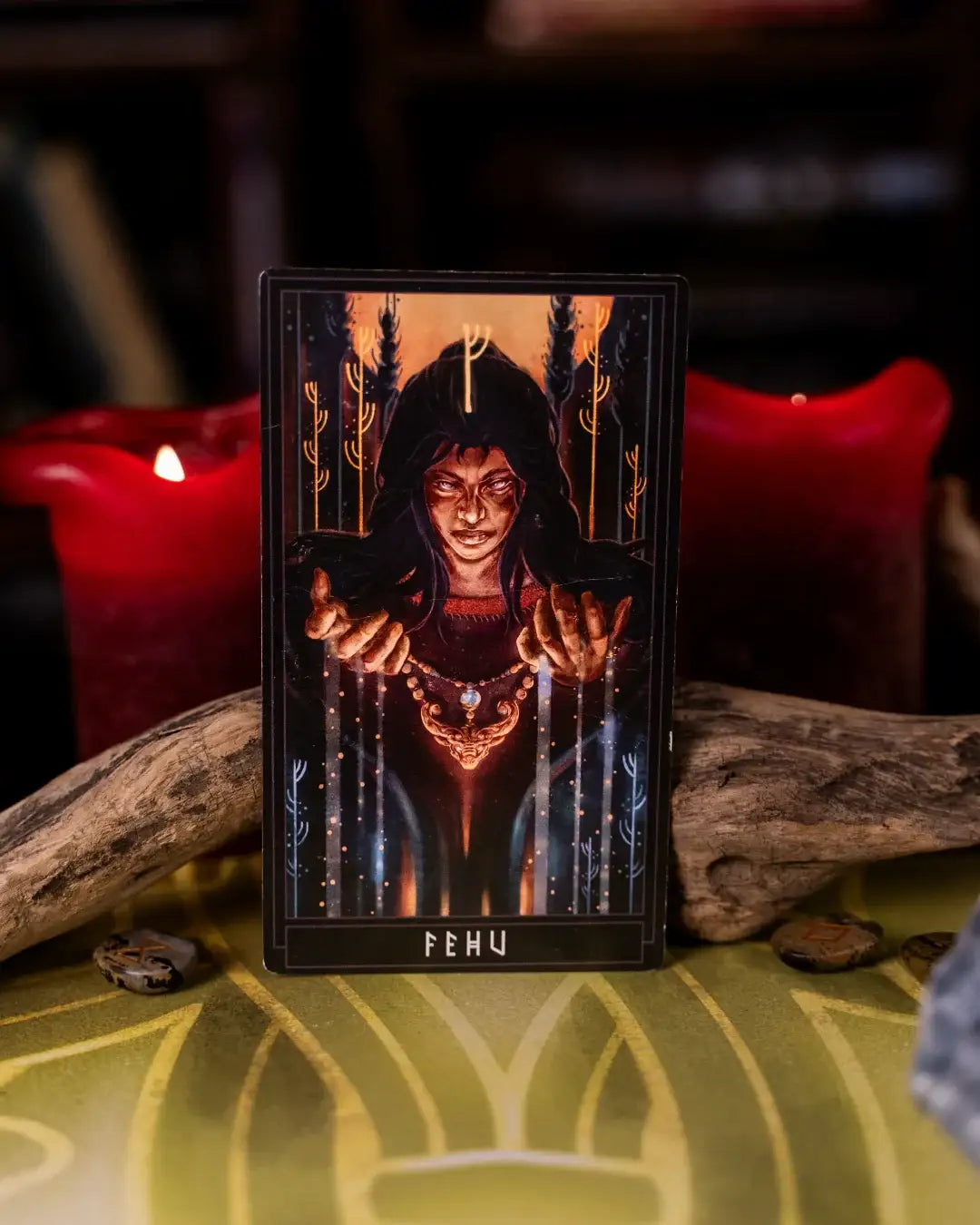 Norse-inspired tarot card featuring Fehu rune, surrounded by candles and runes on a mystical green cloth.
