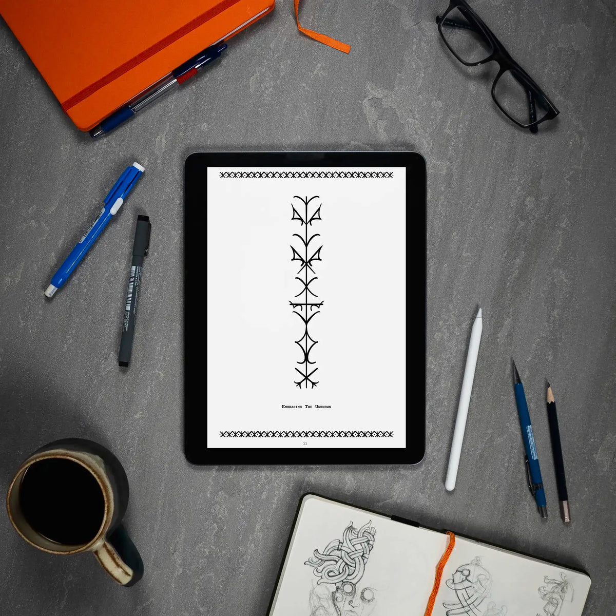 Viking rune tattoo design on tablet, surrounded by sketchbook, pens, and coffee — Norse-inspired art