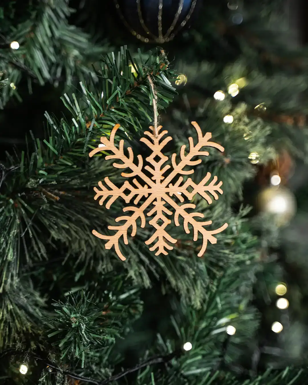 Wooden snowflake ornament hanging on Christmas tree with warm lights