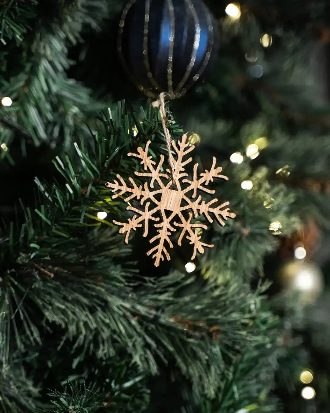 Wooden snowflake ornament hanging on Christmas tree with warm lights