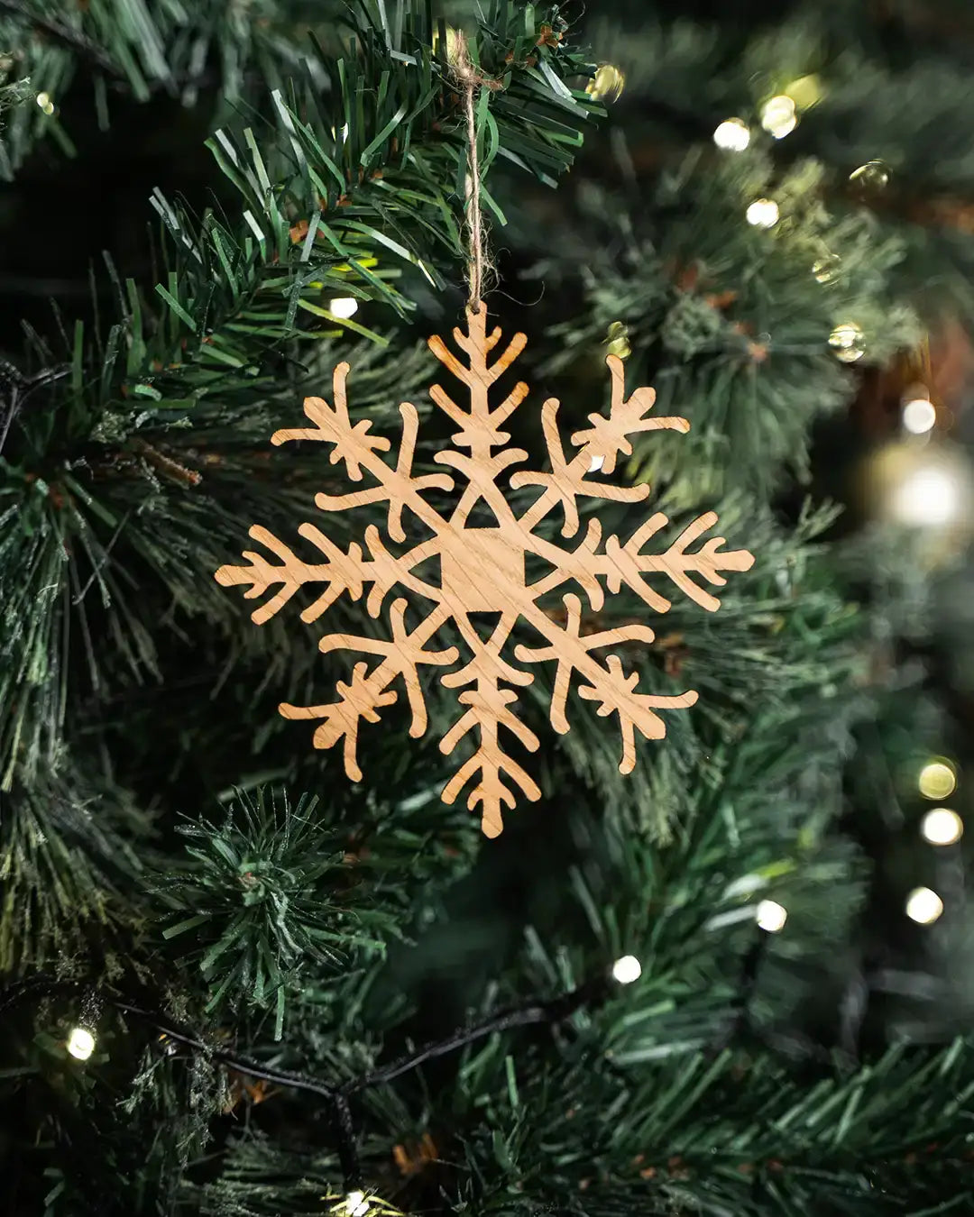 Wooden snowflake ornament hanging on a lit Christmas tree, rustic holiday decor
