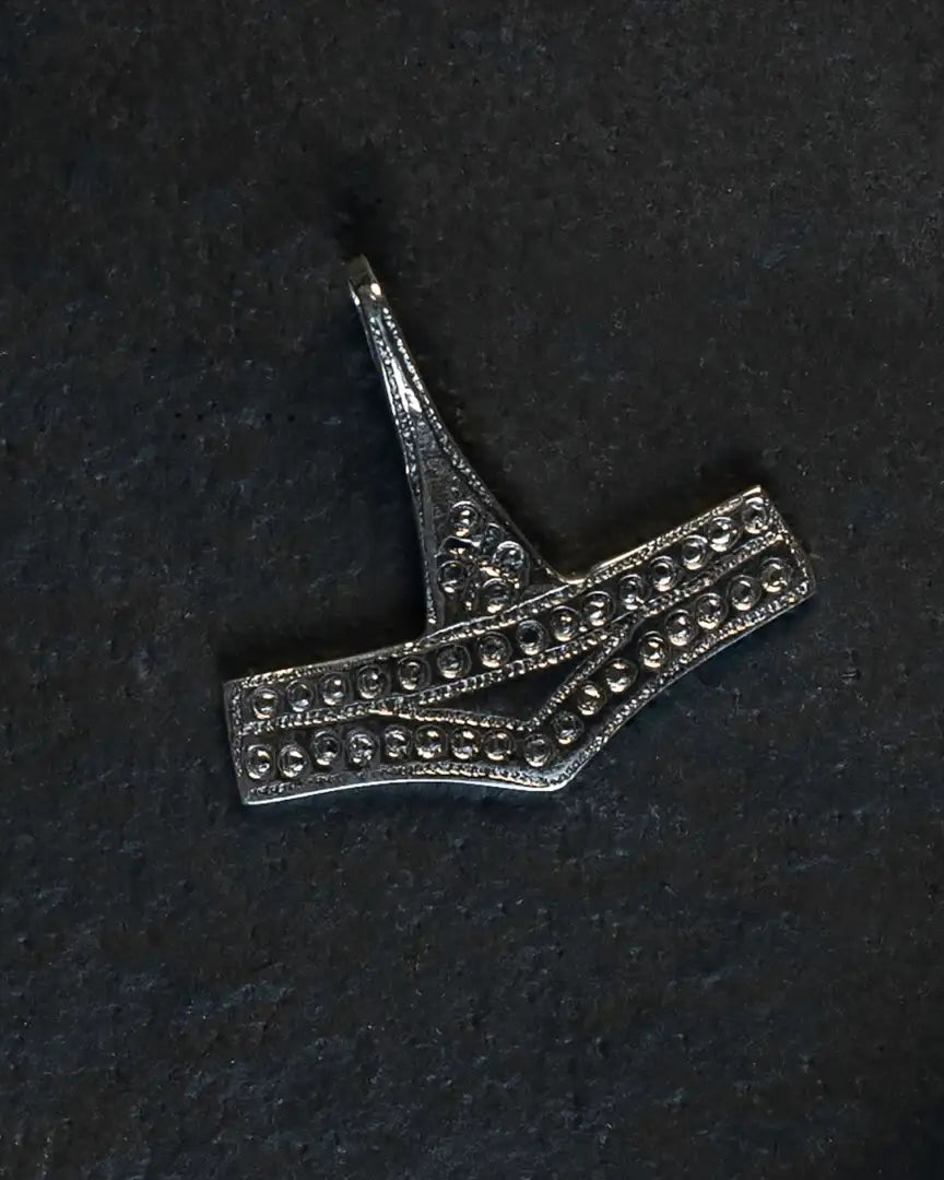 Intricate Norse-inspired metal pendant with dot patterns, styled like Viking-era artifact