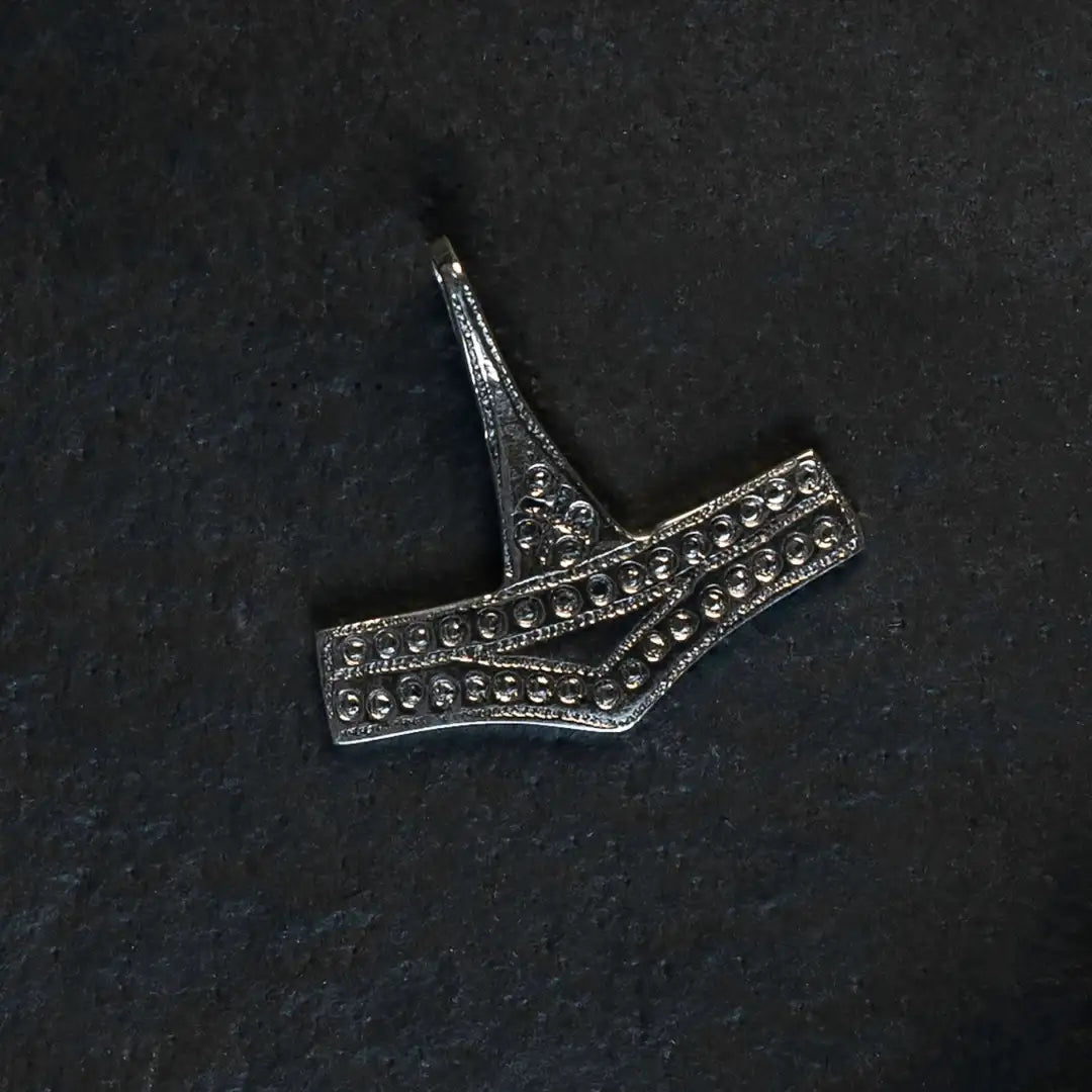 Intricate Norse-inspired metal pendant with dot patterns, styled like Viking-era artifact
