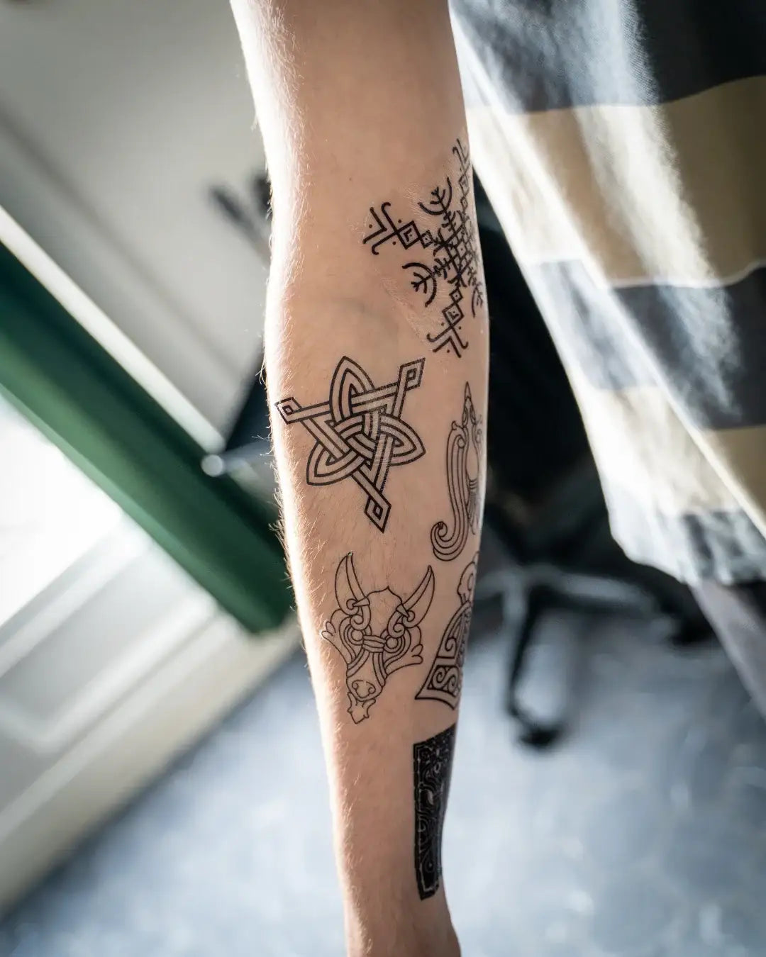 Viking tattoo sleeve featuring Norse runes, Celtic knot, and Odin's helmet design on forearm