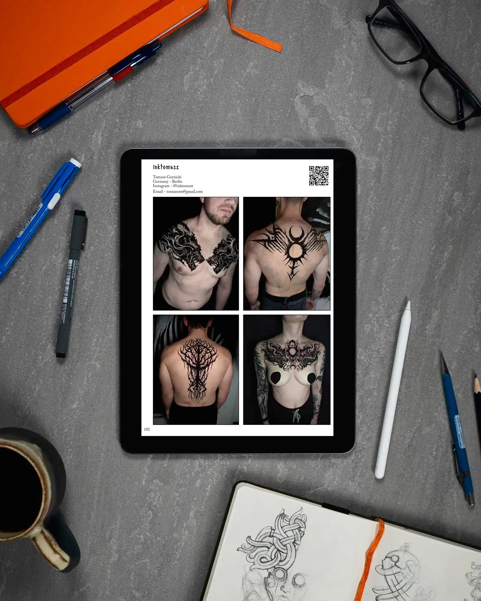 Viking tattoo designs on tablet: Norse-inspired chest, back, and shoulder art with sketchbook and tools nearby