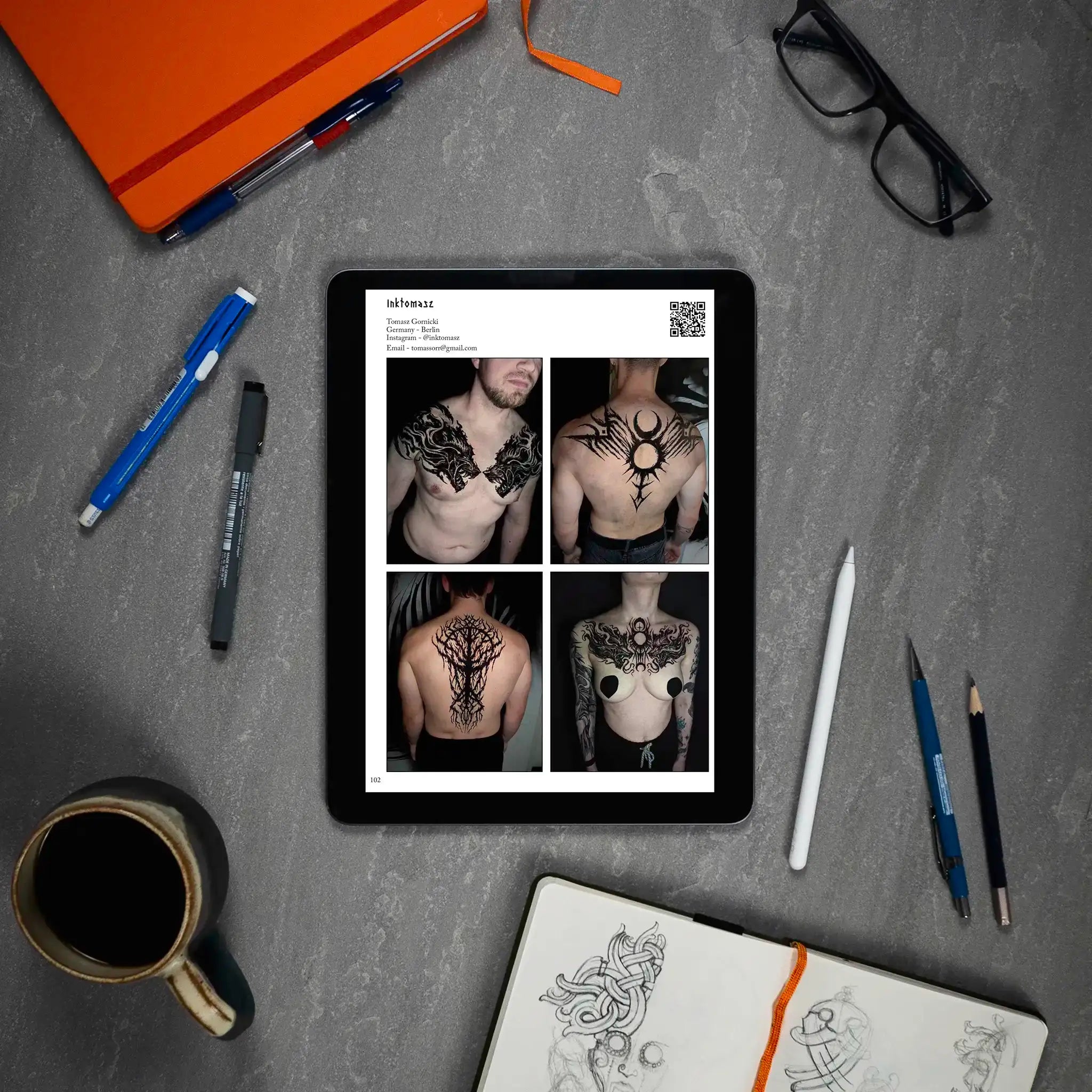 Viking tattoo designs on tablet: Norse-inspired chest, back, and shoulder art with sketchbook and tools nearby
