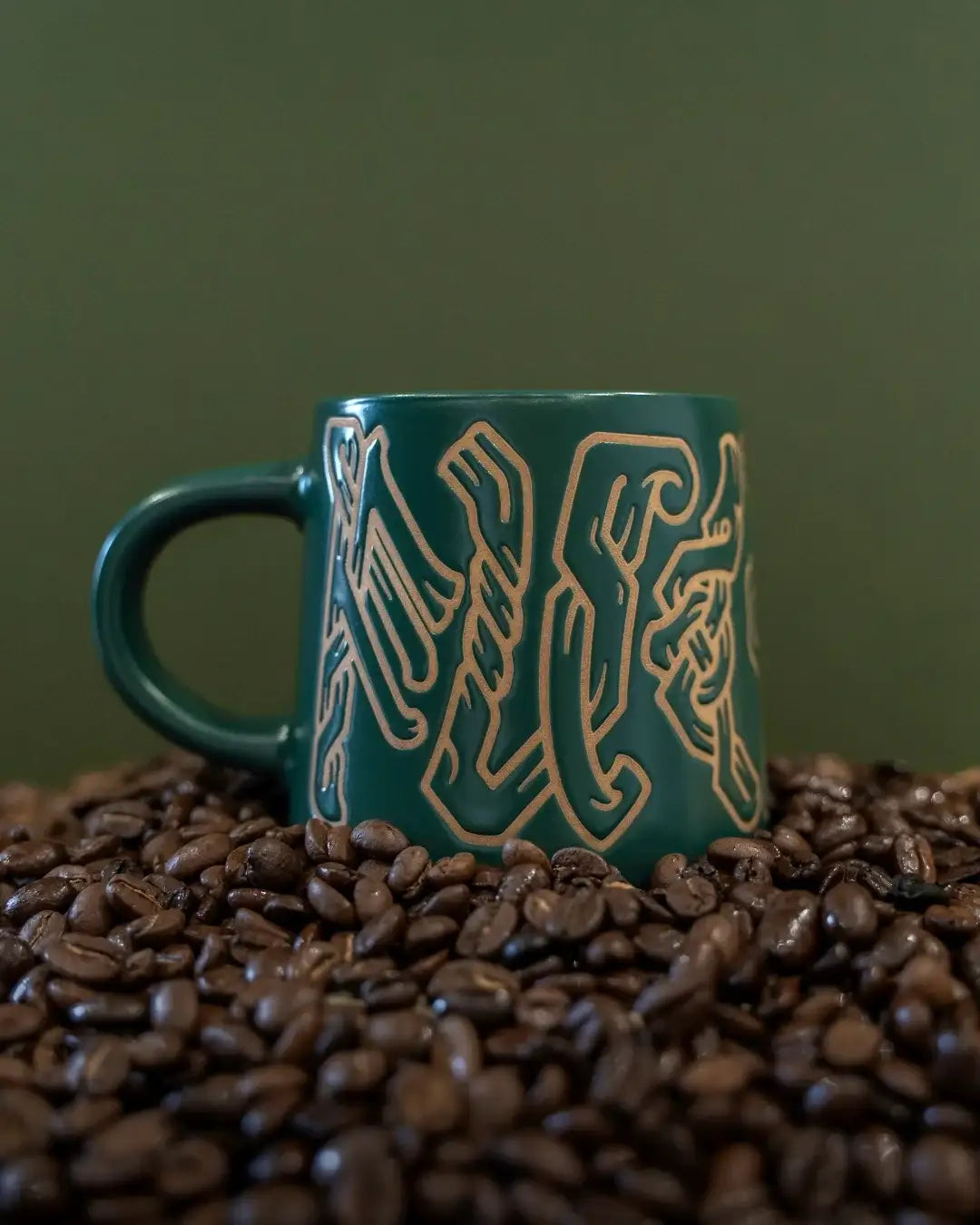 Green mug with Norse knotwork design nestled in coffee beans, Viking-inspired ceramic